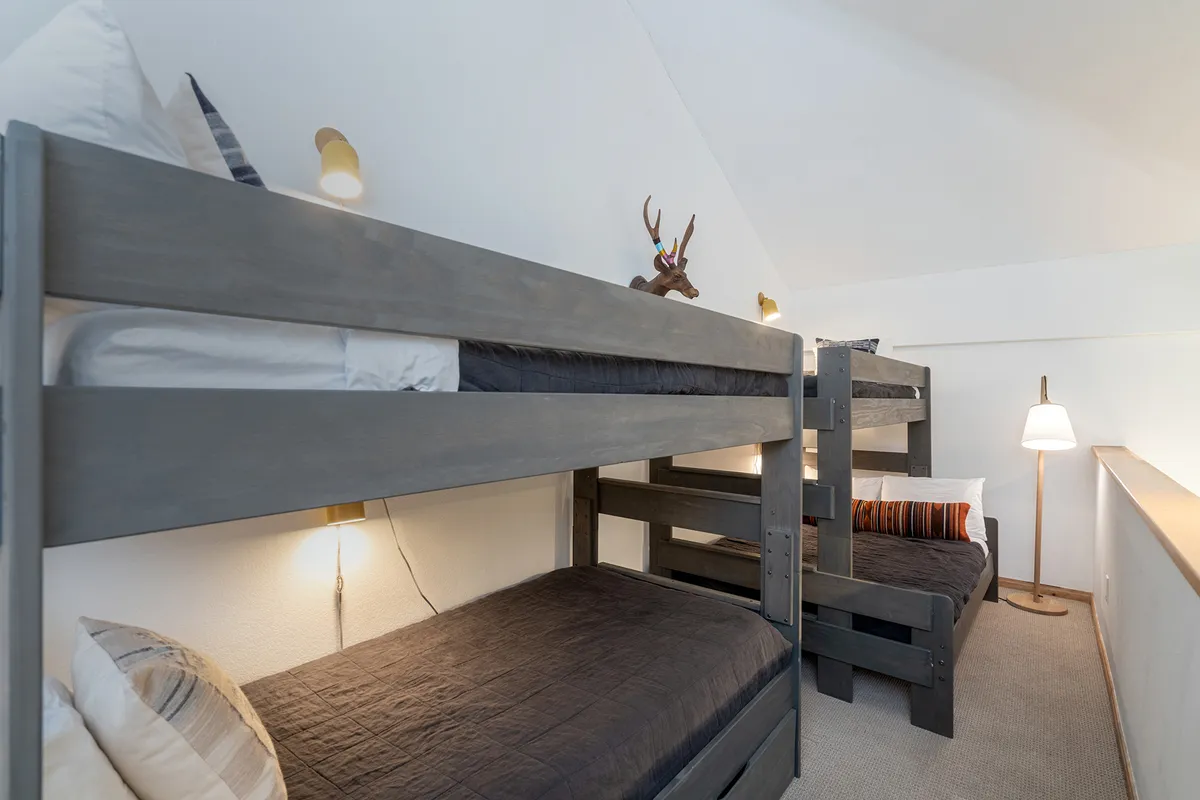 An inviting interior scene features a lofted bunk area with playful decorative antlers and cozy textiles, perfect for kids to retreat to after a day of snowy fun. The lighting feels warm and the mood is relaxed and playful.