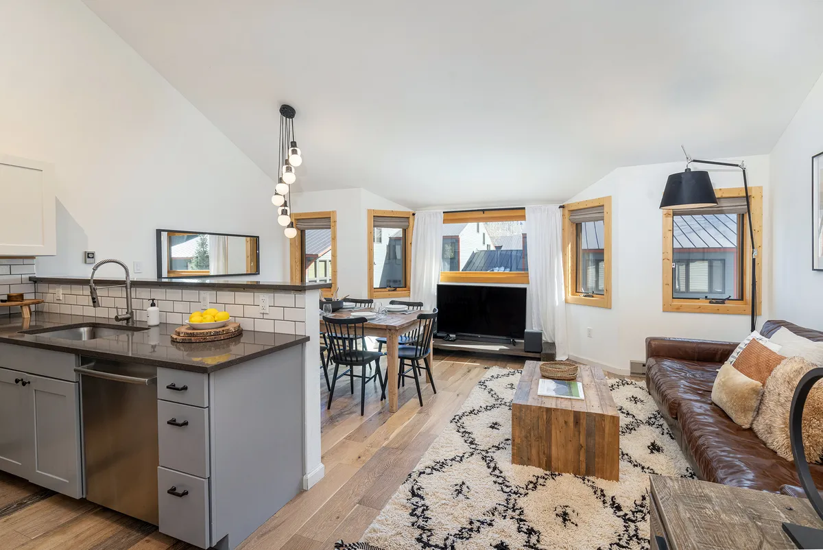 An open-concept interior featuring a modern kitchen island, a well-set dining table, a comfortable leather sofa, and a TV. The kitchen and living spaces are visually connected, promoting interaction and gathering. Subtle lighting and contemporary décor enhance the inviting atmosphere.