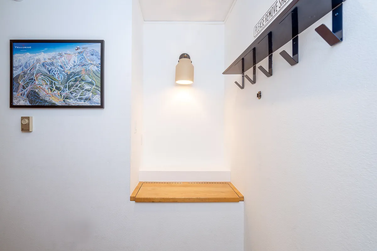 The inviting entryway of the condo features a framed map of Telluride, a sturdy wooden bench, and organized coat hooks, creating a transitional space that bridges outdoor exploration with home comfort. The decor subtly references local geography and adventure.