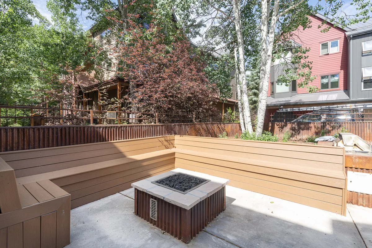 This image shows a cozy fire pit area with ample seating, surrounded by lush greenery. The space is designed for gatherings, relaxation, and stargazing, providing an alternative communal amenity within the complex.
