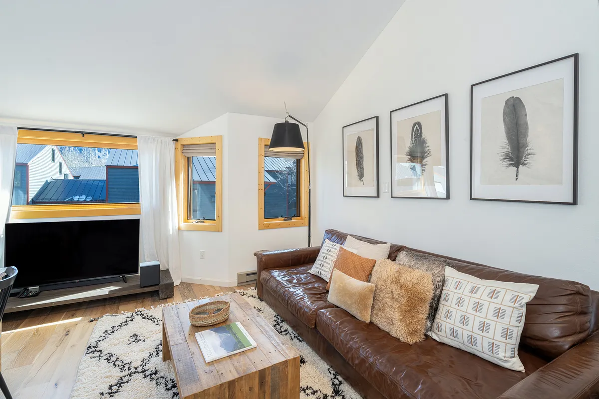 A warm and welcoming living space featuring a leather sofa, a wooden coffee table, large windows letting in ample natural light, and attractive wall art. The room invites relaxation and informal socializing, with comfortable seating perfect for unwinding after outdoor adventures.