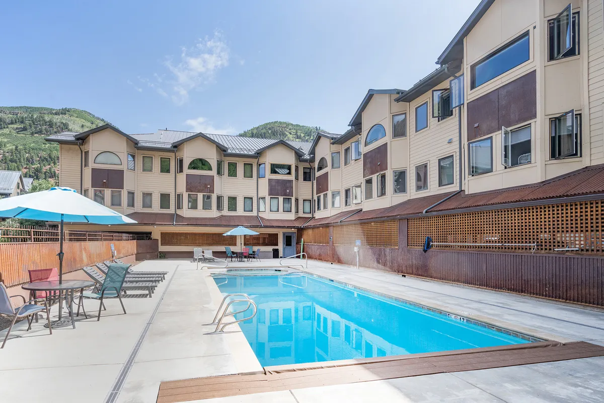 This exterior shot features the shared swimming pool and an outdoor seating area, framed by a striking mountain backdrop. The scene exudes comfort and tranquility, inviting guests to imagine socializing, sunbathing, or enjoying the view.