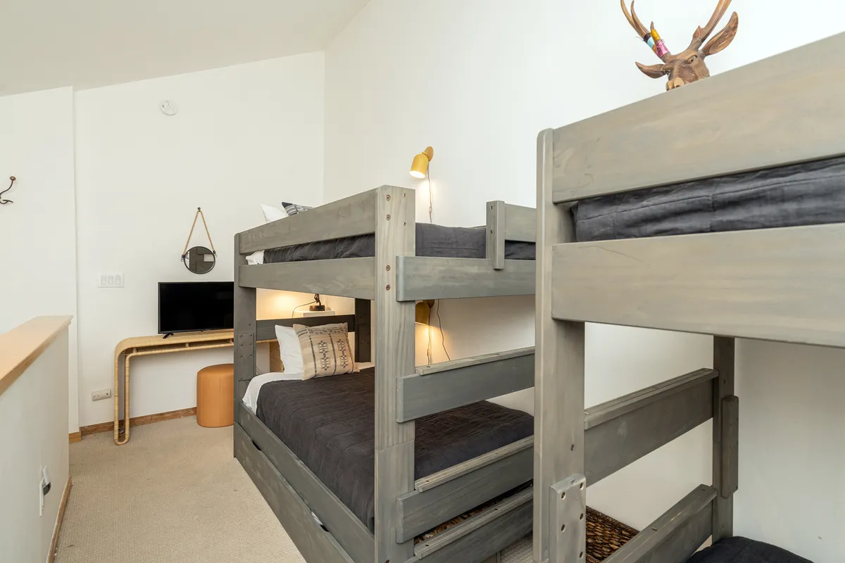 A playful, well-designed loft area with sturdy bunk beds, decorative antlers, a wall-mounted lamp, and a television. The space feels youthful and vibrant, appealing to children or groups, and is ideal for late-night stories, games, and shared adventures.